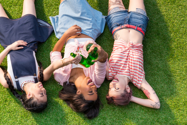багатоетнічні дівчата п'ють пиво на траві
 - Фото, зображення