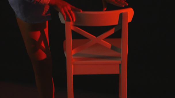 A sexy girl sits on a chair in a In short shorts and a shirt on black background - Footage, Video