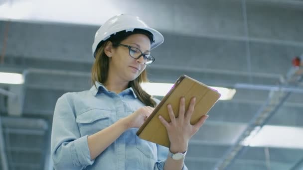Vrouwelijke industrieel ingenieur in een Hard Hat gebruikt Tablet PC terwijl Walking in grote fabriek. - Video