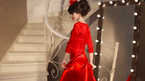 Closeup της μόδας όμορφη νεαρή κοπέλα στη ρετρό καπέλο και κόκκινο φόρεμα, Μελαχρινή μοντέλο με κόκκινα χείλη μακιγιάζ, κομψό χτένισμα, κρεμαστό γυναίκες σετ κοσμημάτων που παρουσιάζουν από καθρέφτη με λάμπες για μακιγιάζ σε σάλτσα - Πλάνα, βίντεο