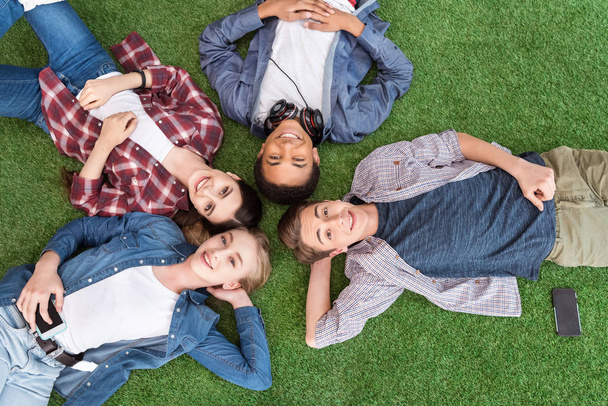 adolescentes multiétnicos tumbados en el césped verde
 - Foto, Imagen