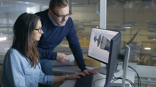 Female Industrial Engineer and Male Project Manager Work on 3D Turbine/ Engine Model in Her CAD Software. Inside of the Factory is Seen From the Office Window. - Footage, Video