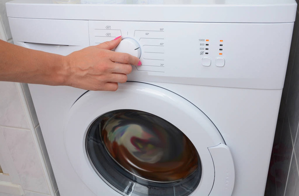 Ver cómo una mujer está encendiendo de la lavadora. Una mujer está eligiendo un modo de lavado en la lavadora
. - Foto, imagen