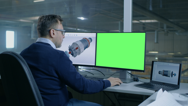 Главный инженер проектирует 3D турбину / двигатель для крупной промышленной компании, его второй дисплей показывает макет зеленого экрана компьютера. Из окна офиса видели большую фабрику
. - Кадры, видео