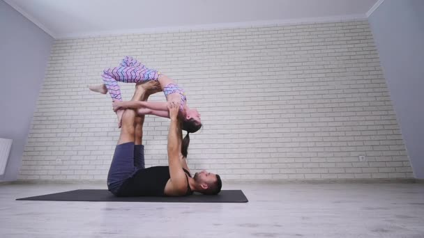 Beautiful couple practicing acro yoga. Young yoga instructors practice in a studio. Two successful young people perform acro yoga exercises - Filmati, video