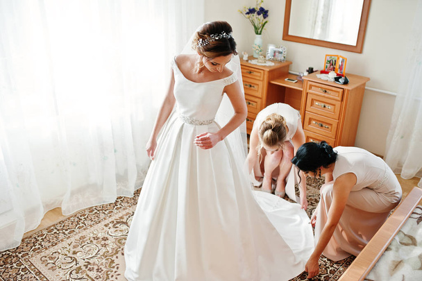Bridesmaids helping gorgeous bride to dress up and get ready for - Fotó, kép