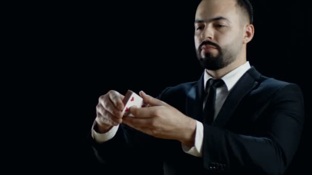 Close-up of a Professional Magician in a Black Suit Performing Card Trick. Throwing and Catching Cards Deck in the Air. Background is Black. Slow Motion. - Séquence, vidéo
