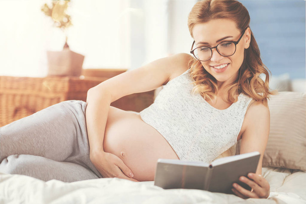 Cheeful pregnant womna reading a book - Zdjęcie, obraz