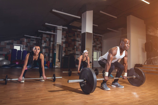 Man and womans standing near heavy barbells in gym. Horizontal indoors shot - Fotó, kép