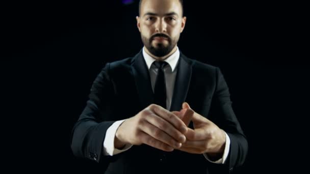 Magician in a Black Suit Steps into the Light does Card Trick Throwing Deck From one Hand to Another. Background is Dark Black. - Video