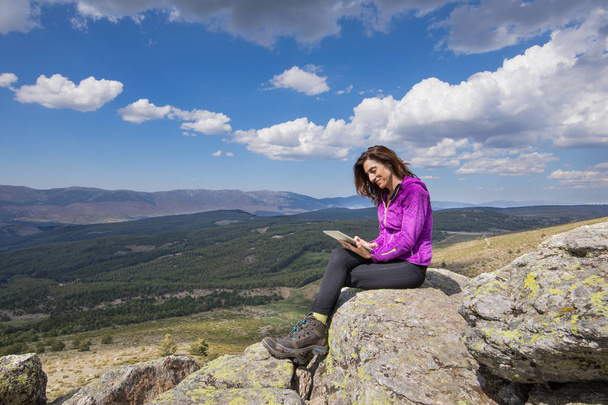 happy woman sitting on top of mountain surfing in tablet - 写真・画像