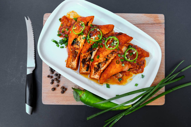 Aziatisch eten Gebakken tofu met champignons en tomaat close-up op een plaat op een tafel. Groene hot chili peppers en groene uien. - Foto, afbeelding