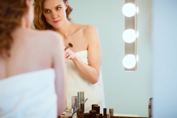 Young woman looking in the mirror and putting make-up on. - Zdjęcie, obraz