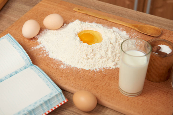 Flour and broken egg closeup for baking on a wooden background. Raw food and kitchen utensils. - Photo, Image