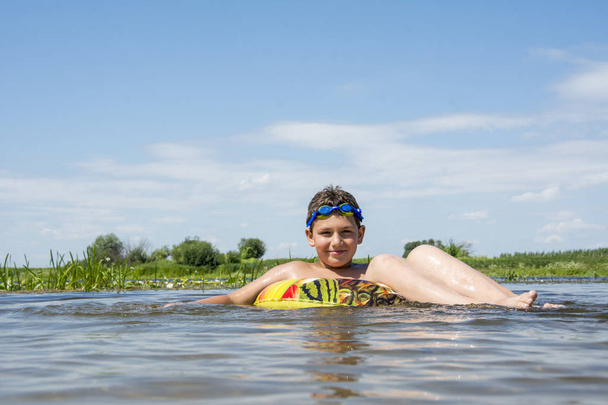 In summer, on a bright, sunny day, a boy swims along the river o - Фото, изображение