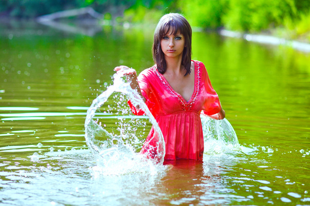 brunette woman red dress is wet to waist in splash water touches - Photo, image