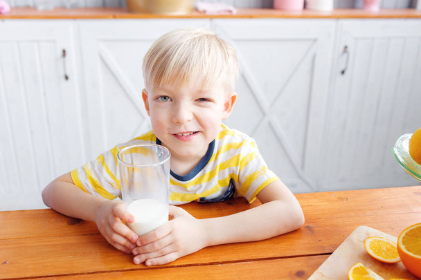 少年は笑みを浮かべてしばらく朝食を食べている、キッチンで。ママはグラスにミルクを注いでください。 - 写真・画像