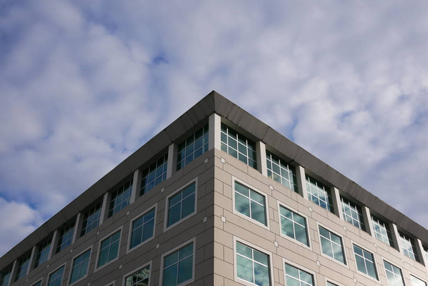 Cielo nublado con fachada de vidrio reflejado iluminado en edificio de oficinas moderno
 - Foto, imagen