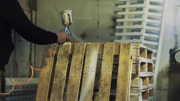 Trabajador usando aspirador para pintar paleta de madera blanca en el taller
 - Imágenes, Vídeo