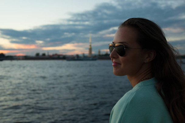 Fiatal és szép lány ül a folyó a rakparton. nézi a naplementét és a hajók mellett elhaladva. Saint Petersburg, Oroszország - Fotó, kép