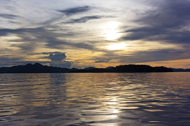 コロン島、フィリピンの地平線上に山に沈む夕日.  - 写真・画像