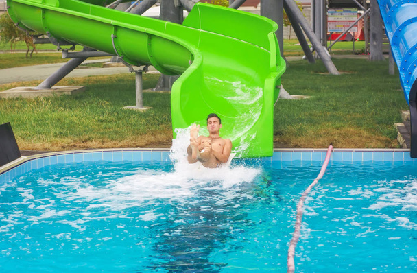 Человек спускается с водной горки к бассейну в аквапарке
.  - Фото, изображение