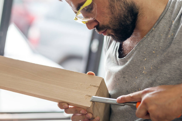человек обрабатывает деревянный продукт зубилом
 - Фото, изображение