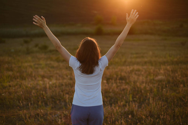 Femme libre levant les bras au coucher de soleil doré. Liberté et succès
 - Photo, image