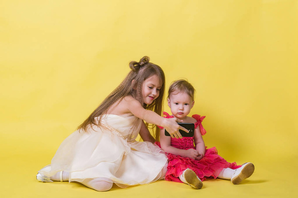 Two sisters in dresses on a yellow background photographed themselves on the phone - Photo, Image