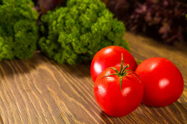 Fresh ripe tomatoes on a wooden table with a green salad on the background. Fresh vegetables. - 写真・画像