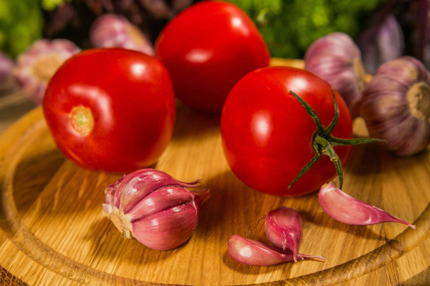 Fresh ripe tomatoes and garlic bulbs on a wooden table with a green salad in the background. Delicious vegetarian food - Foto, Imagem