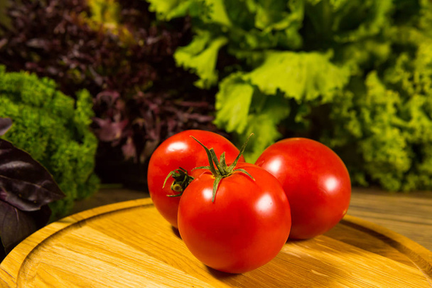 Fresh ripe tomatoes on a wooden table with a green salad on the background. Fresh vegetables. - Zdjęcie, obraz