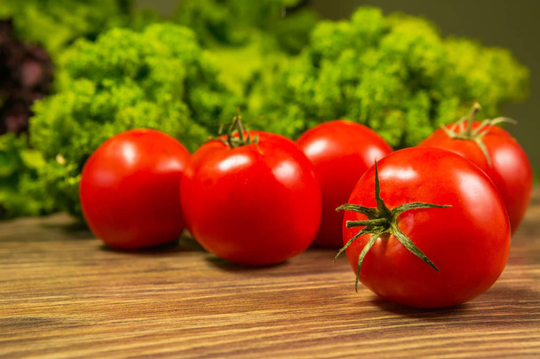 Fresh ripe tomatoes on a wooden table with a green salad on the background. Fresh vegetables. - Фото, зображення