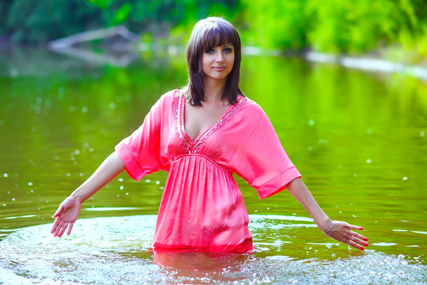 morena mulher modelo vestido vermelho é molhado para cintura em toques de água
 - Foto, Imagem