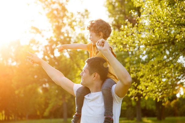 Boy sitting on father shoulders in park - Foto, Bild