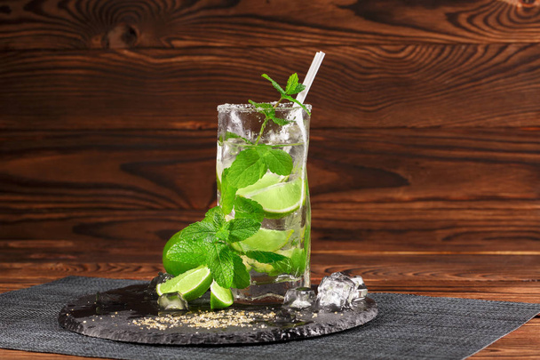 A glass of green mojito. Sour, cold and alcoholic mojito with lime and mint. Alcohol drink on a wooden background. Copy space. - Photo, Image