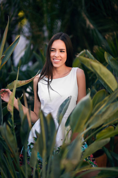 A beautiful and smiling woman. A thoughtful young lady. A girl in a white dress on a green summer park background. A sensual girl. - Foto, imagen