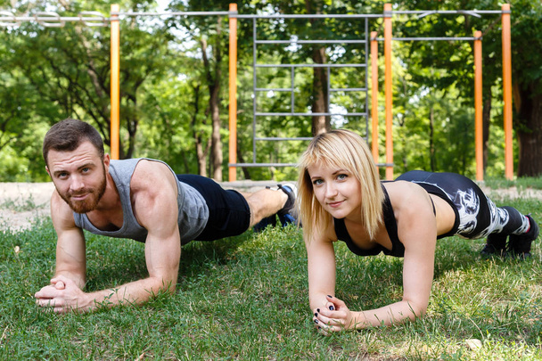 Young attractive couple doing exercise plank in park together. - Fotografie, Obrázek
