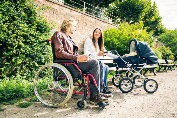 Young Parents In Wheelchair With Baby Stroller In The Park - Foto, afbeelding