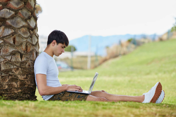 Young man sitting on grass using laptop - 写真・画像