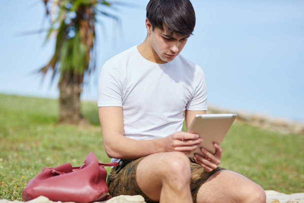 Young man sitting outside using tablet - Foto, afbeelding