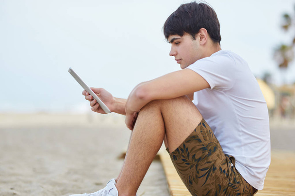 Młody człowiek siedzi na plaży czytania ebook - Zdjęcie, obraz