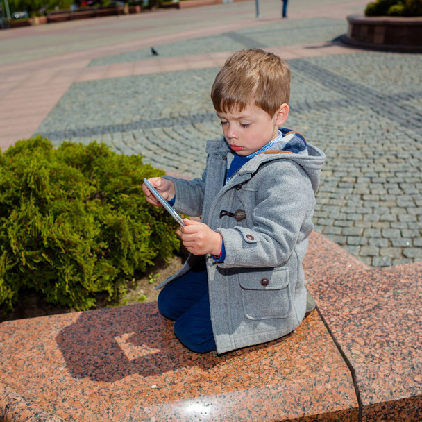 Little boy uses a tablet outdoors - Фото, зображення