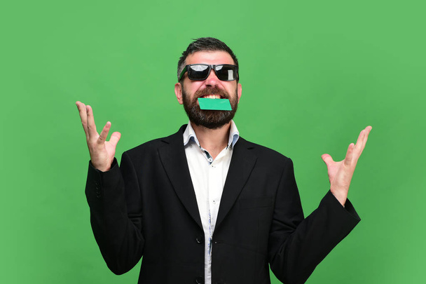 Man with dark beard holds green business card in teeth - Фото, изображение