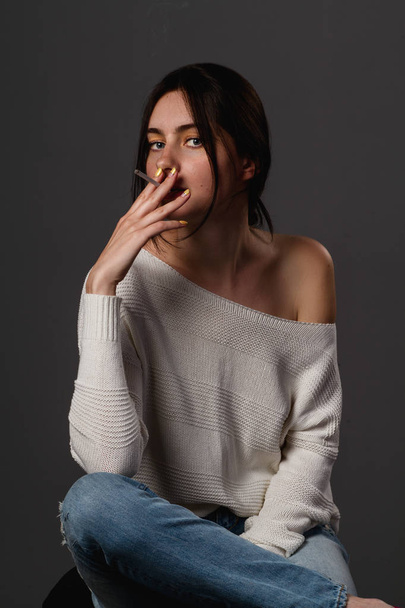 Молодая женщина случайный студийный портрет в белом топе курения
  - Фото, изображение