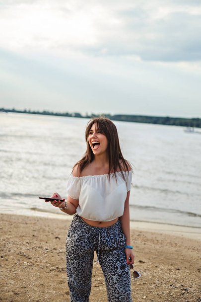 Tyttö nauraa ja pitää puhelimen rannalla
 - Valokuva, kuva