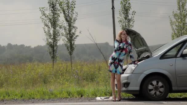 blonde girl calling cellphone in a panic near her broken car with open hood on a country road - Video