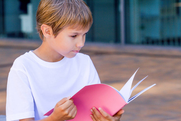 Un colegial leyendo libros. El chico haciendo los deberes al aire libre. Regreso al concepto escolar
. - Foto, imagen