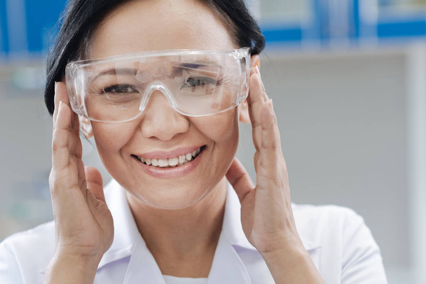 Delighted laboratory scientist fixing her protective glasses - 写真・画像