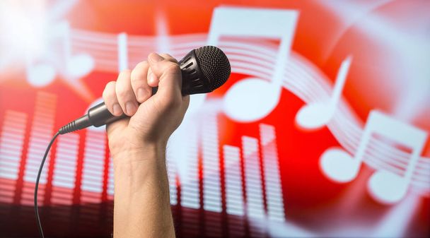 Conceito de canto, karaoke ou treinamento vocal. Microfone na mão na frente de uma música abstrata tema nota e fundo equalizador
.  - Foto, Imagem